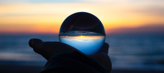 clear orb being held reflecting the ocean during sunset