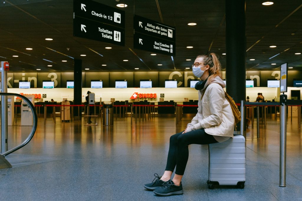 new normal | a woman sits in an empty airport check-in lobby with a mask on her face during covid-19