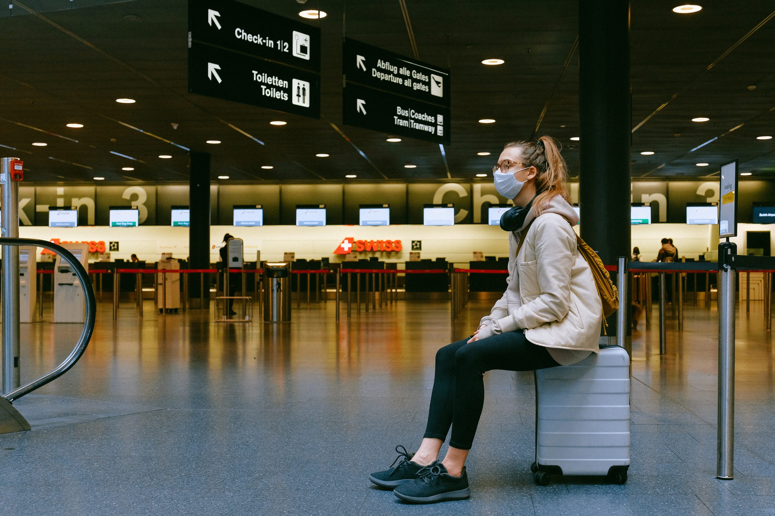 new normal | a woman sits in an empty airport check-in lobby with a mask on her face during covid-19