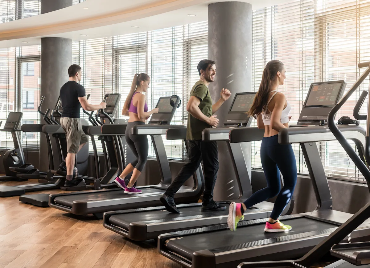 Group of four people, men and women, running on treadmills in modern and luminous fitness gym