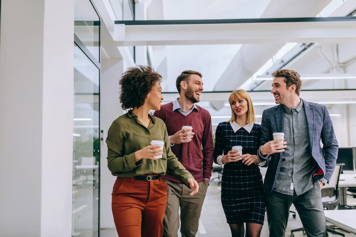 Group of diverse coworkers walking through a corridor in an office, holding paper cups