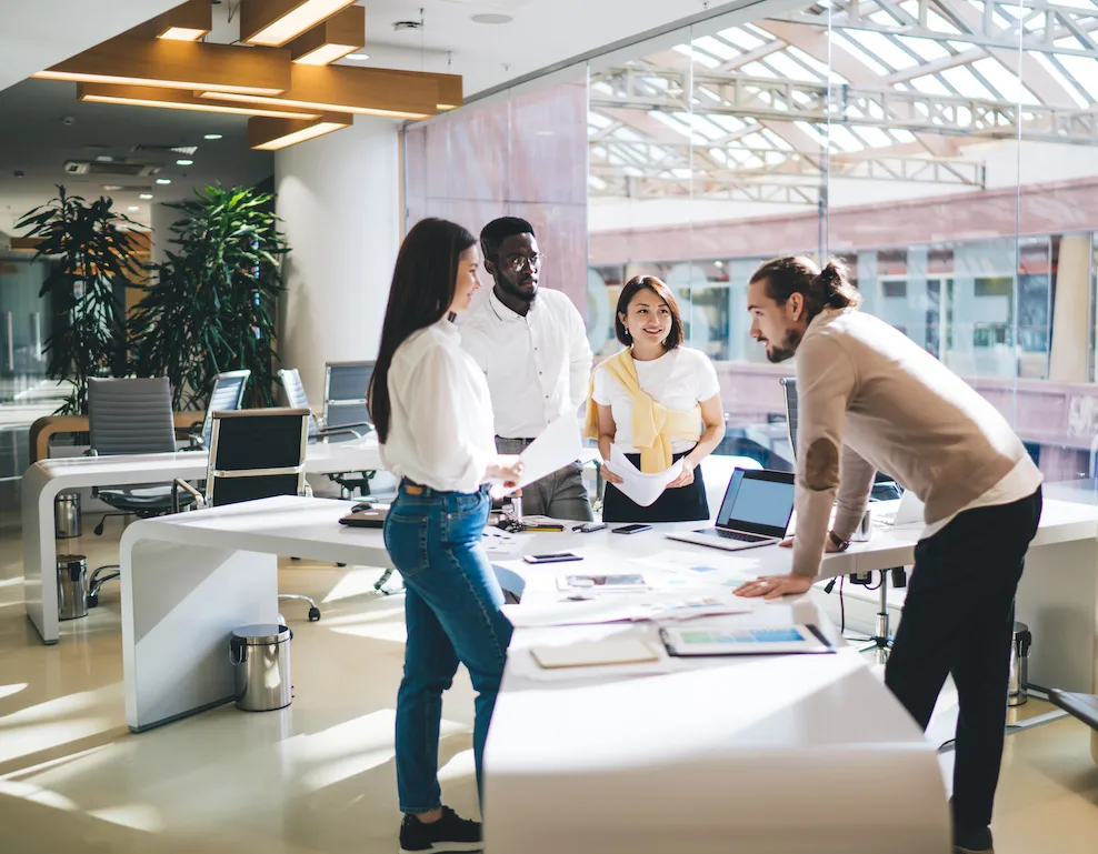 Successful male and female colleagues discussing business solutions during brainstorming meeting, young multiracial partners standing near table desktop talking and analyzing financial documents