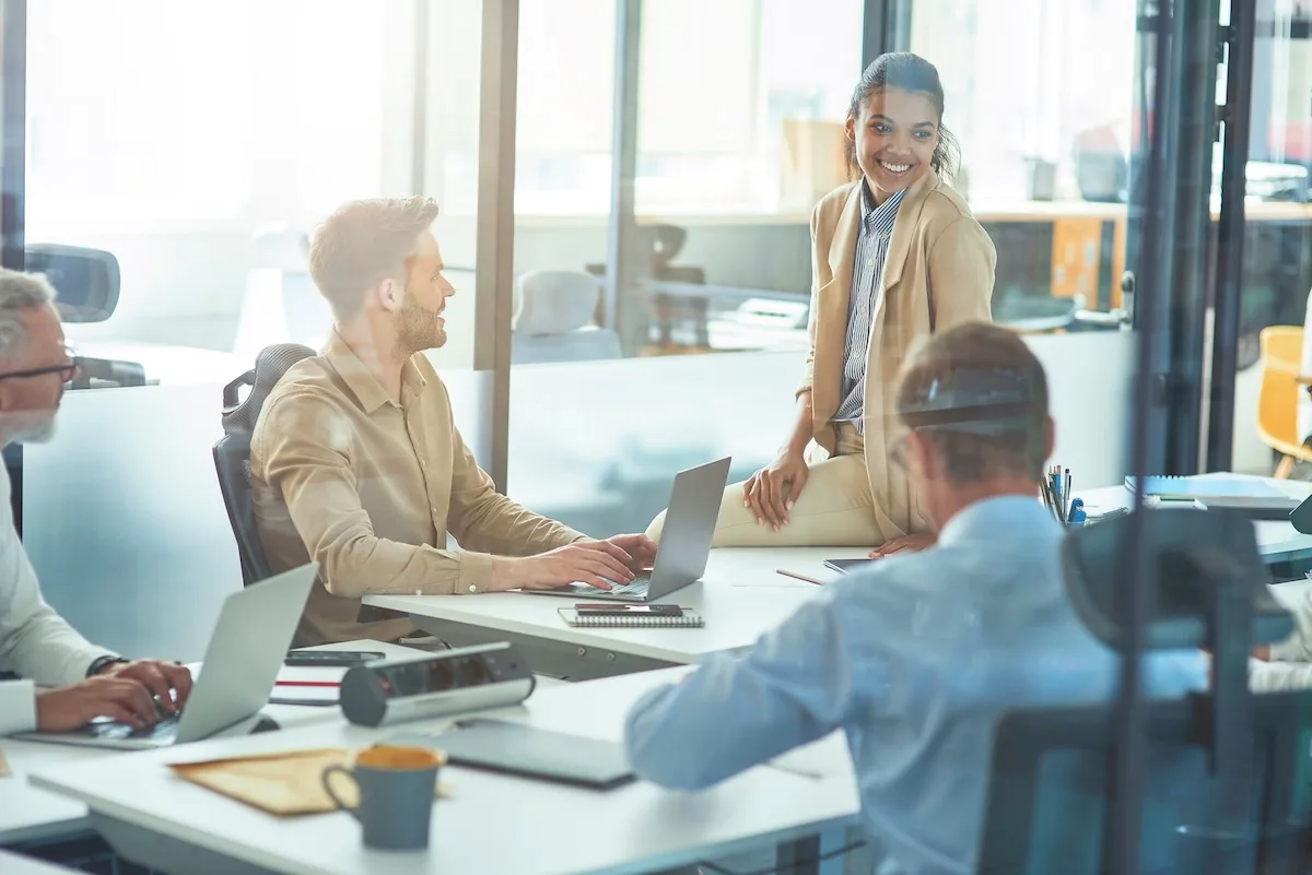 Young cheerful mixed race female office worker discussing something with colleagues while sitting in board room in the modern office, business people having a meeting. Teamwork and business concept